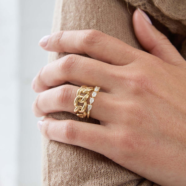 Close up of a hand wearing Zoe Chicco 14k gold and diamond rings on a light background