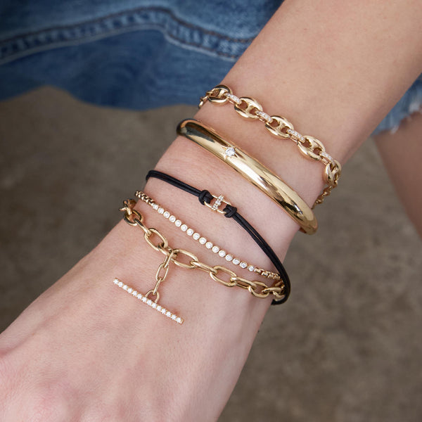 woman's wrist wearing a Zoë Chicco 14k Gold 3 Prong Diamond Link Leather Cord Bracelet stacked with a Small Diamond Bezel Tennis Segment Box Chain Bracelet, 14k Extra Large Square Oval Chain Pavé Diamond Toggle Bracelet, 14k Single Star Set Diamond Small Aura Cuff, and a 14k Mixed Small & Large Mariner Chain with Diamond Links Bracelet