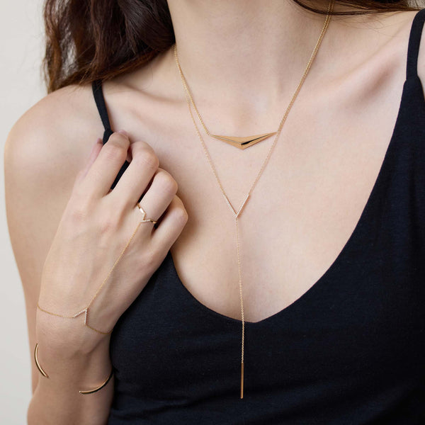 Woman wearing layered Zoe Chicco 14k gold necklaces and ring hand chain on a plain background