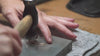 Close up of a person hammering Zoe Chicco 14k gold into flat hoop earrings on a desk with tools