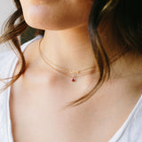 woman wearing Zoë Chicco 14kt Gold Itty Bitty Pave Diamond Heart Necklace, Itty Bitty LOVE Necklace, and a Garnet Pendant Necklace