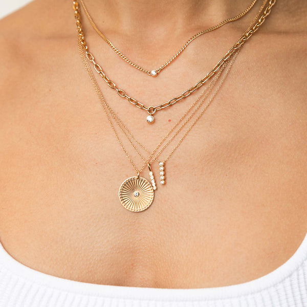 woman in white tank top wearing Zoë Chicco 14kt Gold Extra Small Curb Chain Bezel Diamond Necklace layered with Medium Square Oval Link Dangling Diamond Bezel Necklace, Vertical 5 Diamond Bezel Bar Necklace, and other gold and diamond necklaces