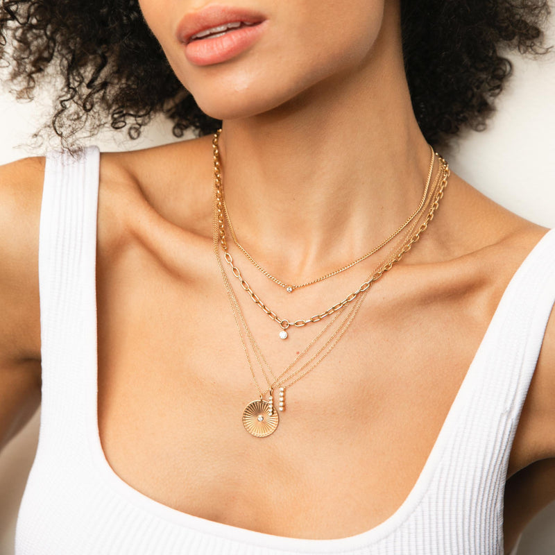 woman in white tank top wearing Zoë Chicco 14kt Gold Extra Small Curb Chain Bezel Diamond Necklace layered with Medium Square Oval Link Dangling Diamond Bezel Necklace and other gold and diamond necklaces