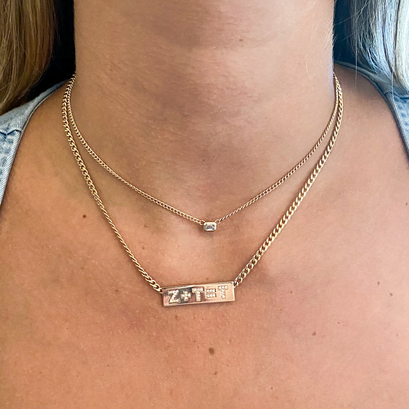 close up of woman wearing an initial equation ID necklace and an emerald cut diamond necklace