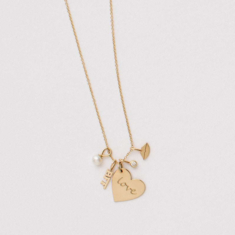 flat lay of Zoë Chicco 14kt Gold LOVE Medium Heart Charm Pendant on a chain with four other Zoe Chicco charms