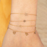 close up of wrist wearing Zoe Chicco 14kt Gold Initial Letter Bracelets stacked with Itty Bitty Bracelets