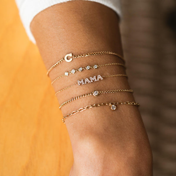 woman's wrist wearing Zoë Chicco 14kt Gold Initial Letter XS Curb Chain Bracelet stacked with 5 Linked Floating Diamond Bracelet and other diamond bracelets
