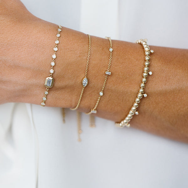 woman's wrist wearing Zoë Chicco 14kt Gold Bead Bracelet with Dangling Diamond Bezels layered with three diamond bracelets
