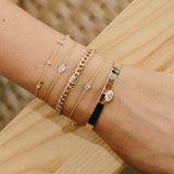 woman's wrist on a wooden background wearing Zoë Chicco 14kt Gold Paris Mixed Diamond Station Bracelet stacked with fancy cut diamond bracelets