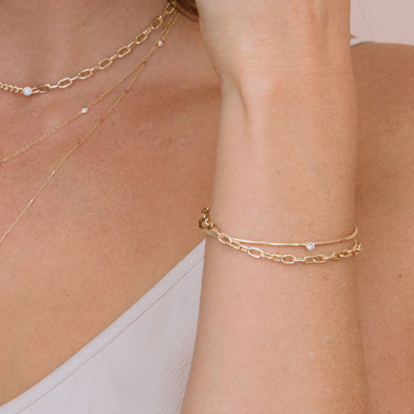 close up of woman's wrist wearing Zoë Chicco 14k Gold Prong Diamond Cuff & Medium Square Oval Chain Double Bracelet