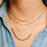 woman wearing Zoë Chicco 14kt Gold Extra Small Curb Chain Bezel Diamond Necklace layered with Gold Bead necklaces and a Graduated Diamond Bezel Necklace