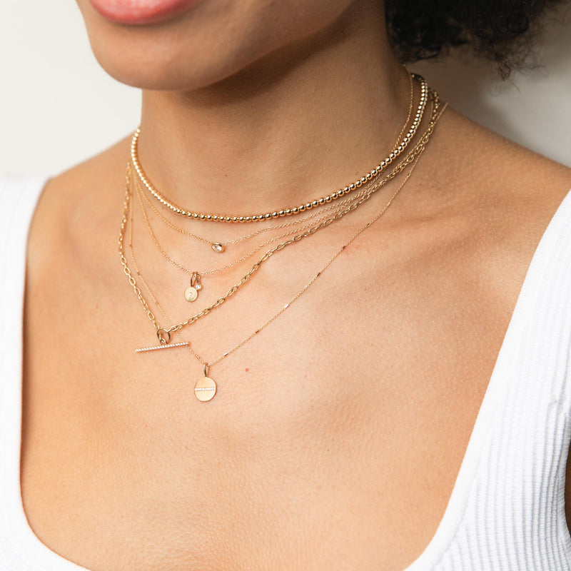 woman in white tank top wearing Zoe Chicco 14k Gold Small Gold Bead Necklace,, Midi Bitty Diamond Disc & Diamond Bezel Charm Necklace layered with a Small Square Oval Link Chain Pavé Diamond Toggle Necklace and Pave Diamond Line Disc Necklace