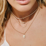 close up of a woman wearing a Zoë Chicco 14k Gold Mixed Cut Diamond Brushed Gold Shield Pendant Necklace layered with two diamond necklaces and a pearl choker