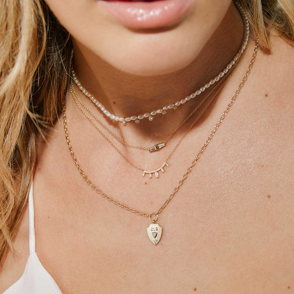 a woman in a white camisole wearing a Zoë Chicco 14k Gold Double Tapered Baguette Diamond Necklace layered with a pearl and diamond choker and a Zoë Chicco 14k Gold Graduated Baguette Diamond Curved Bar Necklace