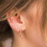 woman's ear with a diamond ear cuff, two diamond studs, and a dangling gold and diamond link earring
