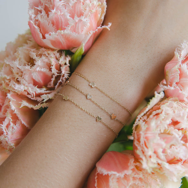 wrist wearing Zoë Chicco 14kt Gold Itty Bitty Heart Bracelets with pink flowers in the background