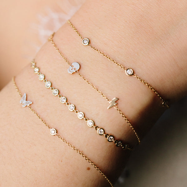woman's wrist wearing Zoë Chicco 14kt Gold Itty Bitty Skull, Star, & Lightning Bolt Bracelet stacked with floating diamond bracelets