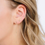 close up of woman's ear wearing princess cut diamond stud earrings and gold diamond shaped earrings