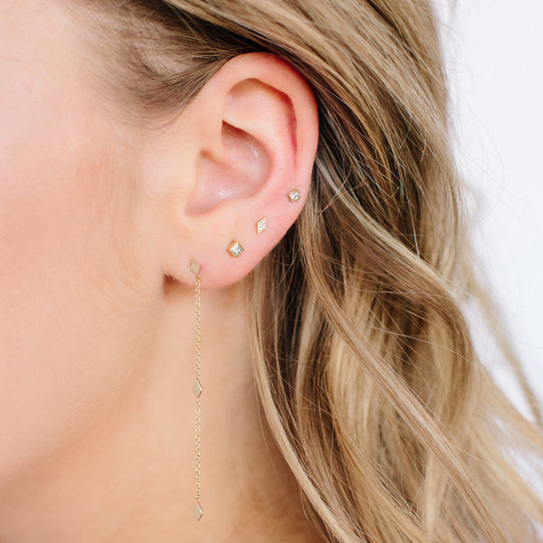 close up of woman's ear wearing princess cut diamond stud earrings and gold diamond shaped earrings