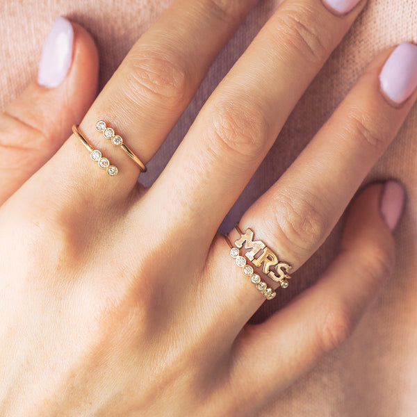 woman's hand wearing Zoe Chicco 14kt gold 7 Diamond Bezel Ring and MRS and diamond ring stacked on her fourth finger with a Diamond Bezel Wrap ring on her index finger