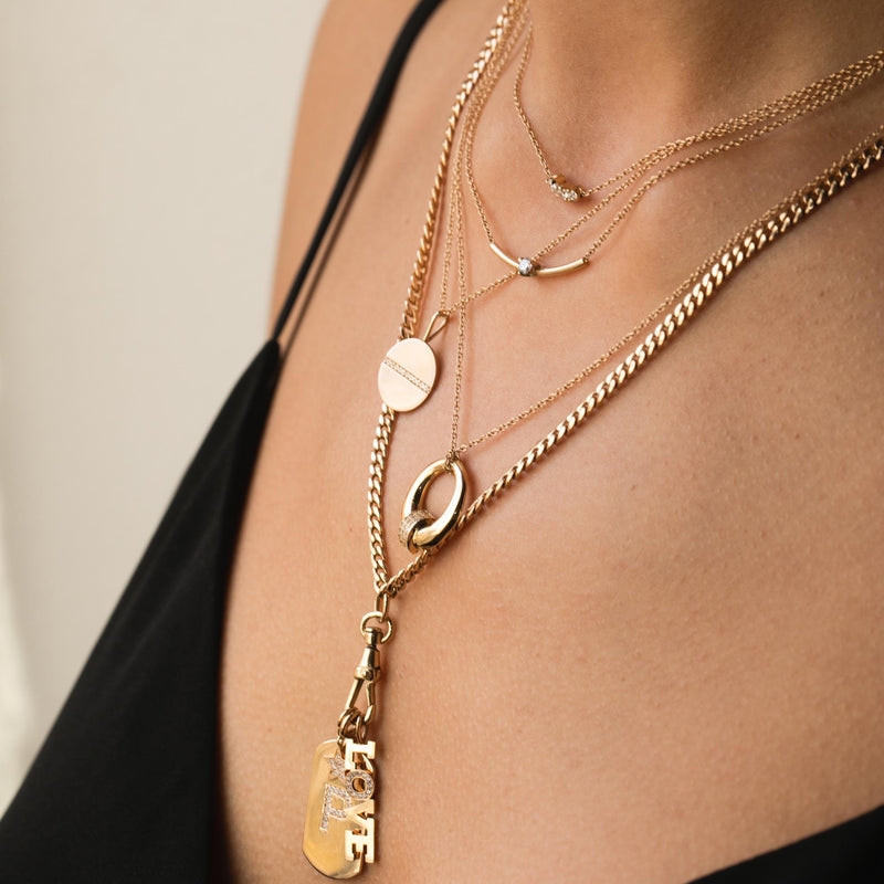 woman in black top wearing a Zoë Chicco 14k Medium Pavé Diamond Line Disc Pendant Necklace layered with other necklaces