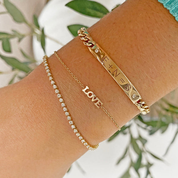 woman's wrist wearing Zoë Chicco 14kt Gold Itty Bitty LOVE Bracelet with a diamond tennis bracelet and a personalized 2 Diamond Equation bracelet