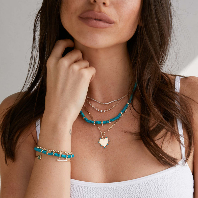 woman in white tank top wearing a Zoë Chicco 14k Gold 7 Prong Turquoise Heart Pendant on Small Square Oval Chain Necklace layered with other necklaces