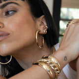 woman with hand resting on her shoulder wearing Zoë Chicco 14k Gold Large Tube Hoop Earrings layered with Chubby huggie hoops and ear cuffs