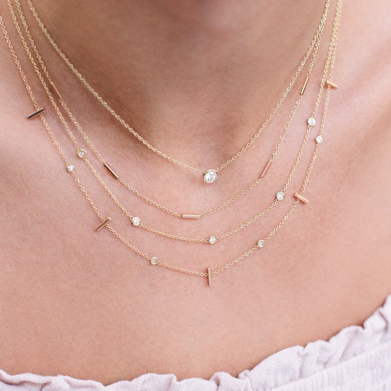 close up of woman wearing Zoë Chicco 14kt Gold 5 Tiny Bar Station Necklace layered with three other necklaces