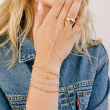 woman in a denim jacket holding her wrist up wearing a Zoë Chicco 14k Gold Floating Diamond Mixed Curb Chain & Diamond Tennis Bracelet layered with three other diamond bracelets and a hand chain