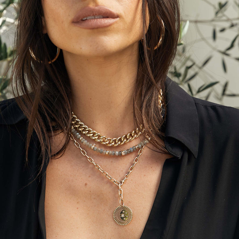 woman in black top wearing a Zoë Chicco 14k Gold & Labradorite Rondelle Bead Necklace with 5 Prong Diamonds and  Large Diamond Celestial Protection Medallion Oval Chain Necklace with a leaf background