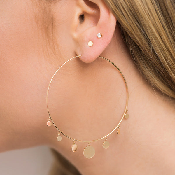 woman's ear with Zoe Chicco diamond stud earring, itty bitty round disc stud earring, and a graduated disc extra large hoop earring