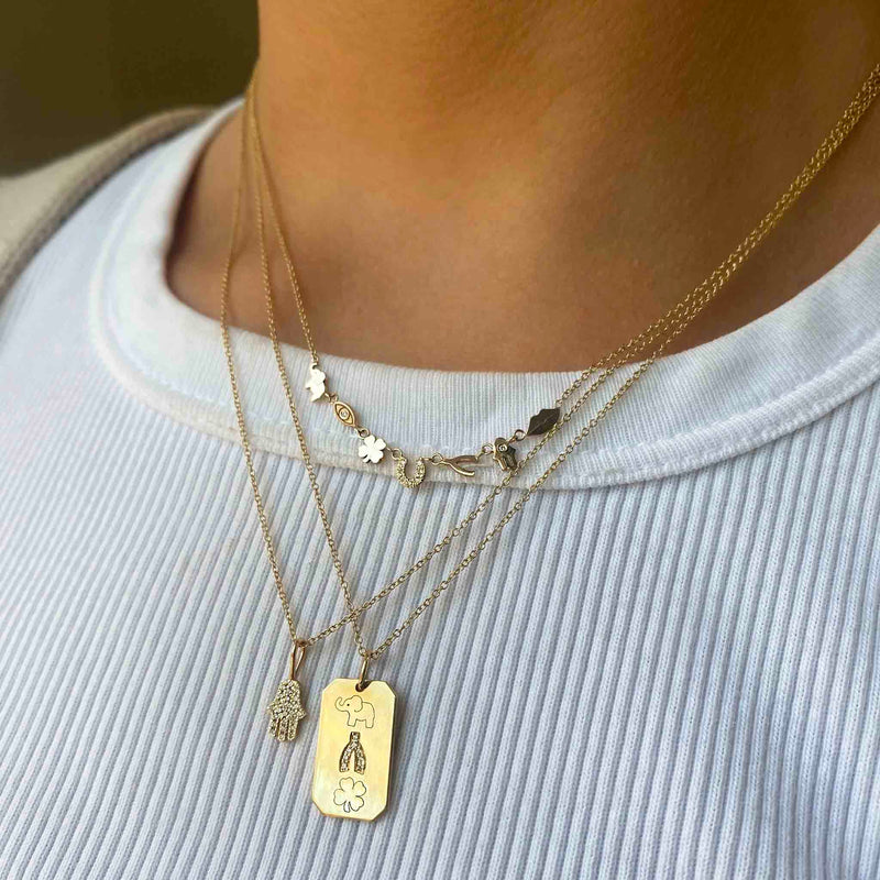 woman in white top wearing a Zoë Chicco 14k Gold 7 Itty Bitty Gold & Diamond Linked Luck Symbols Necklace layered with a Pave Diamond Hamsa Pendant Necklace and Lucky Medium Square Edge Dog Tag Necklace