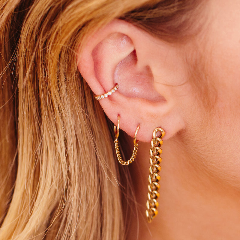 woman's ear wearing a Zoë Chicco 14k Gold Extra Small Curb Chain Double Huggie Hoop Earring layered with a Curb Chain drop earring and a Diamond Bezel Eternity Ear Cuff