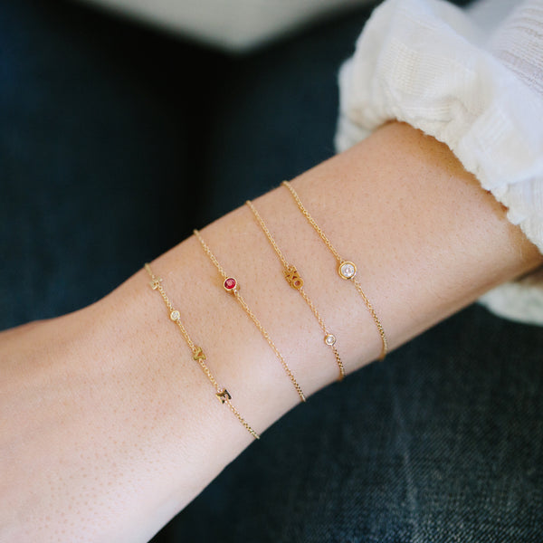 woman's wrist wearing Zoe Chicco 14kt Gold Single Bezel Ruby Bracelet stacked with a Love bracelet, XO bracelet, and floating diamond bracelet