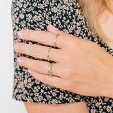 woman resting hand on a floral shirt wearing Zoë Chicco 14kt Gold 12 Scattered Pave Diamond Band Ring on her middle finger and plain gold bands