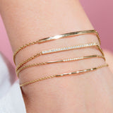 woman's wrist wearing Zoë Chicco 14kt Gold 10 Pave Diamond Bar Bracelet layered with three other bar bracelets