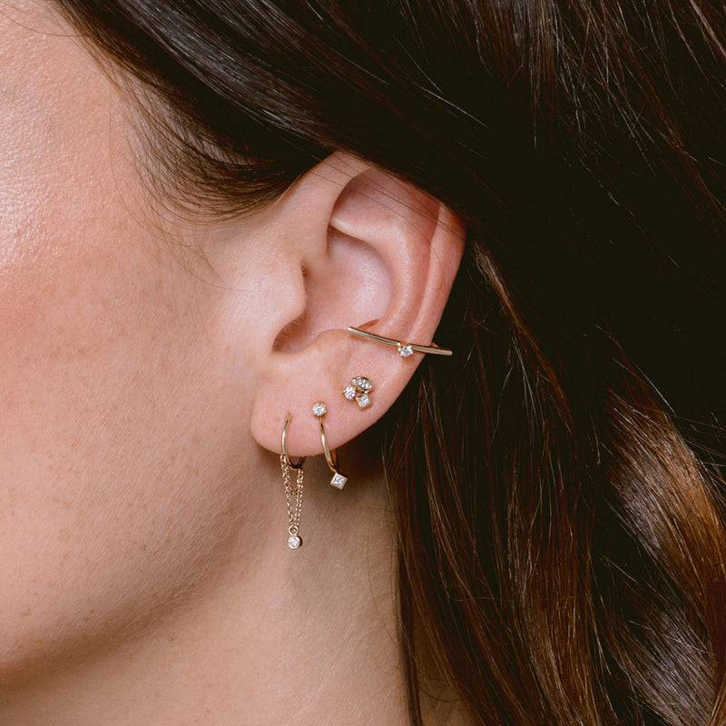 close up of woman's ear wearing Zoë Chicco 14k Gold Double Chain Loop Thin Huggie Hoops with Dangling Diamond Bezel