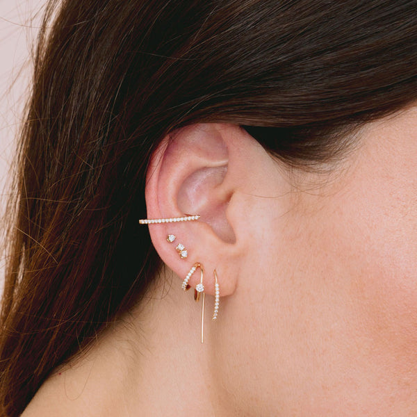close up of woman's ear wearing Zoë Chicco 14k Gold Pavé Diamond Thick Wire Bar Ear Cuff stacked with other diamond earrings