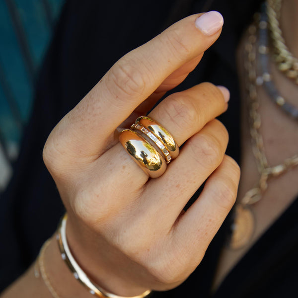 woman's hand wearing a Zoe Chicco 14k Gold Half Round Wide Band Ring, Baguette Diamond Eternity Band, and a Medium Aura Ring stacked together