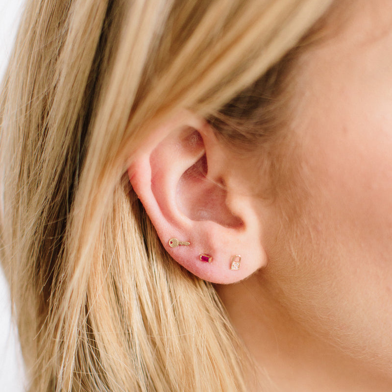 a blonde woman's ear wearing a Zoë Chicco 14k Gold Itty Bitty Key Stud Earring in her third piercing