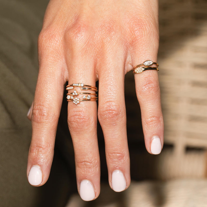 close up of woman's hand wearing a Zoe Chicco 14k Gold Tapered Baguette Diamond & Prong Diamond Ring, Baguette & Pavé Diamond Open Ring,  stacked with other diamond rings and 2 signet rings