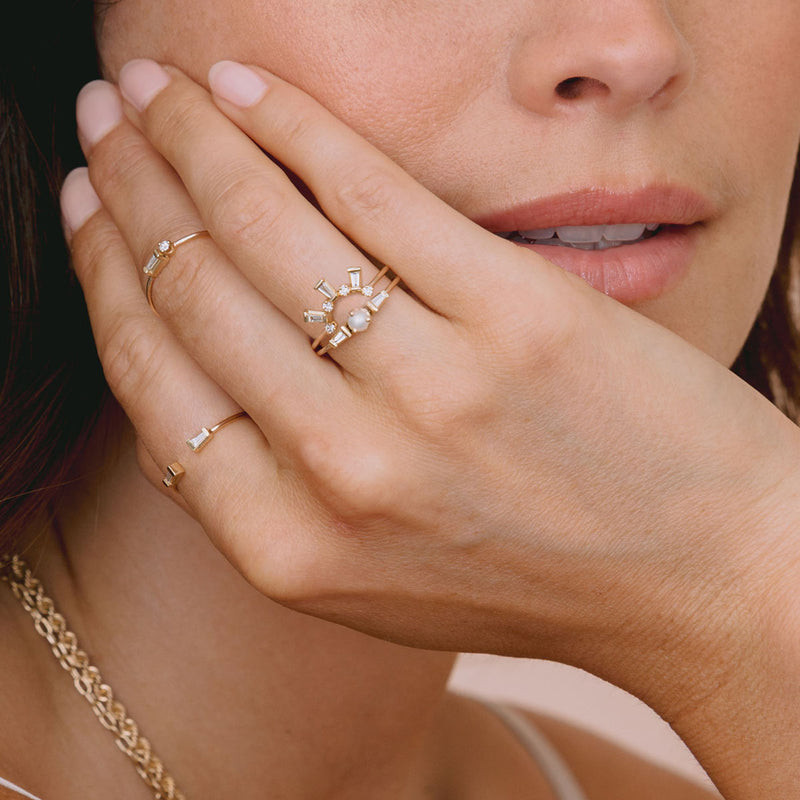woman's hand resting on face wearing Zoë Chicco 14k Gold Tapered Baguette & Prong Diamond Curved Bar Ring on her fourth finger