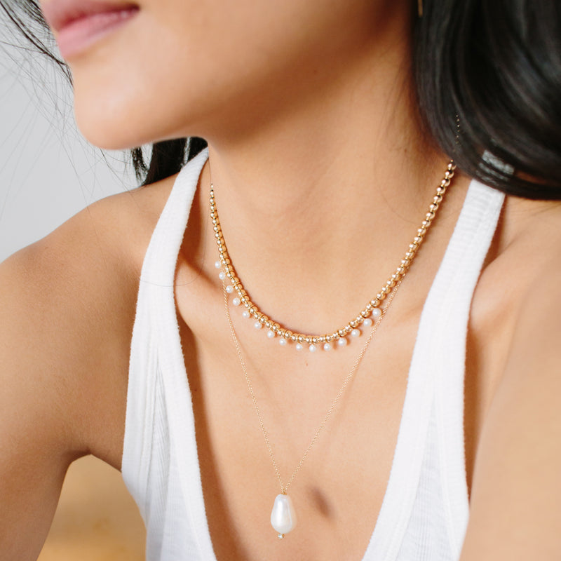 woman wearing Zoe Chicco 14kt Gold Baroque Pearl and Prong Diamond Necklace layered with a Gold Bead Eternity and Tiny Pearl Necklace