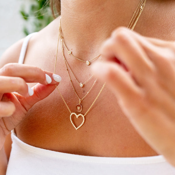 woman wearing Zoë Chicco 14kt Gold Pave Diamond Heart Disc Necklace layered with a diamond heart necklace and two floating diamond necklaces