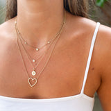 woman in white camisole top wearing a Zoë Chicco 14k Gold Floating Graduated Diamond Station Necklace layered with a Floating Diamond Necklace, Diamond Bezel Heart Necklace, and a Pave Diamond Heart Disc Pendant Necklace