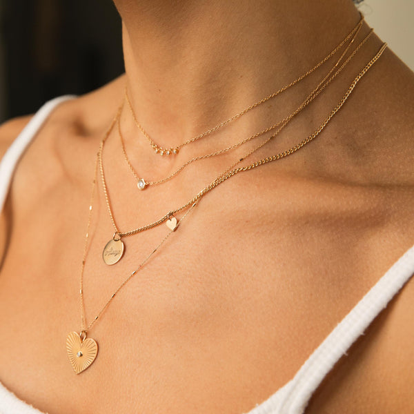 woman in white top wearing Zoë Chicco 14kt Gold Linked 5 Diamond Bezel Necklace layered with a Floating Diamond Necklace, Amore Pendant with Heart Curb Chain Necklace, and a Radiant Heart Medallion Bar and Cable Chain Necklace