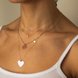 woman in white top wearing Zoë Chicco 14kt Gold Linked 5 Diamond Bezel Necklace layered with a Floating Diamond Necklace, Amore Pendant with Heart Curb Chain Necklace, and a Radiant Heart Medallion Bar and Cable Chain Necklace