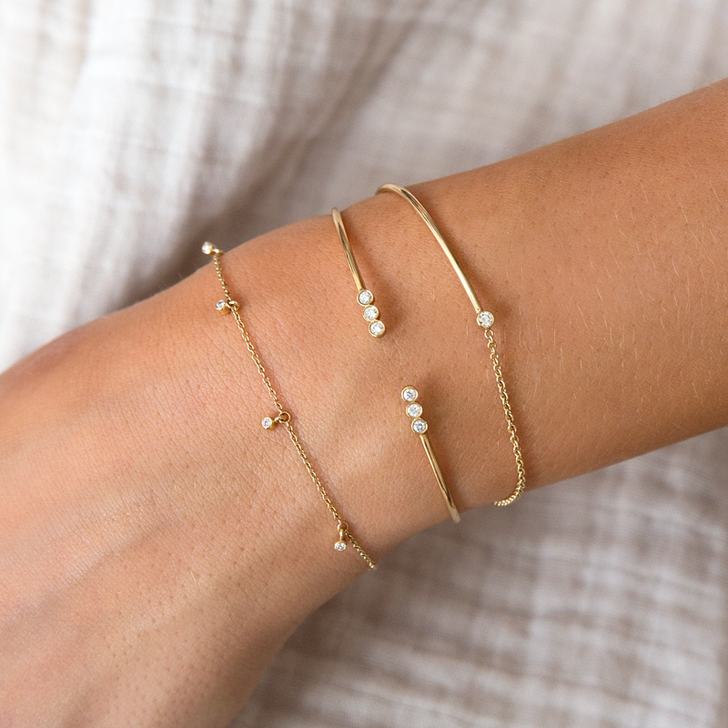 woman's wrist wearing a stack of Zoe Chicco 14kt Gold and Diamond Bezel Chain Bracelets and Cuff