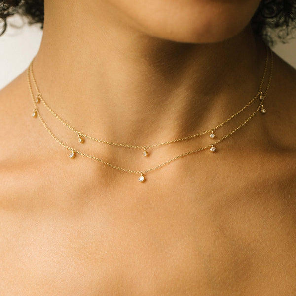 woman wearing two Zoë Chicco 14k Gold 5 Dangling Diamond Bezel Necklaces with two different diamond sizes layered together